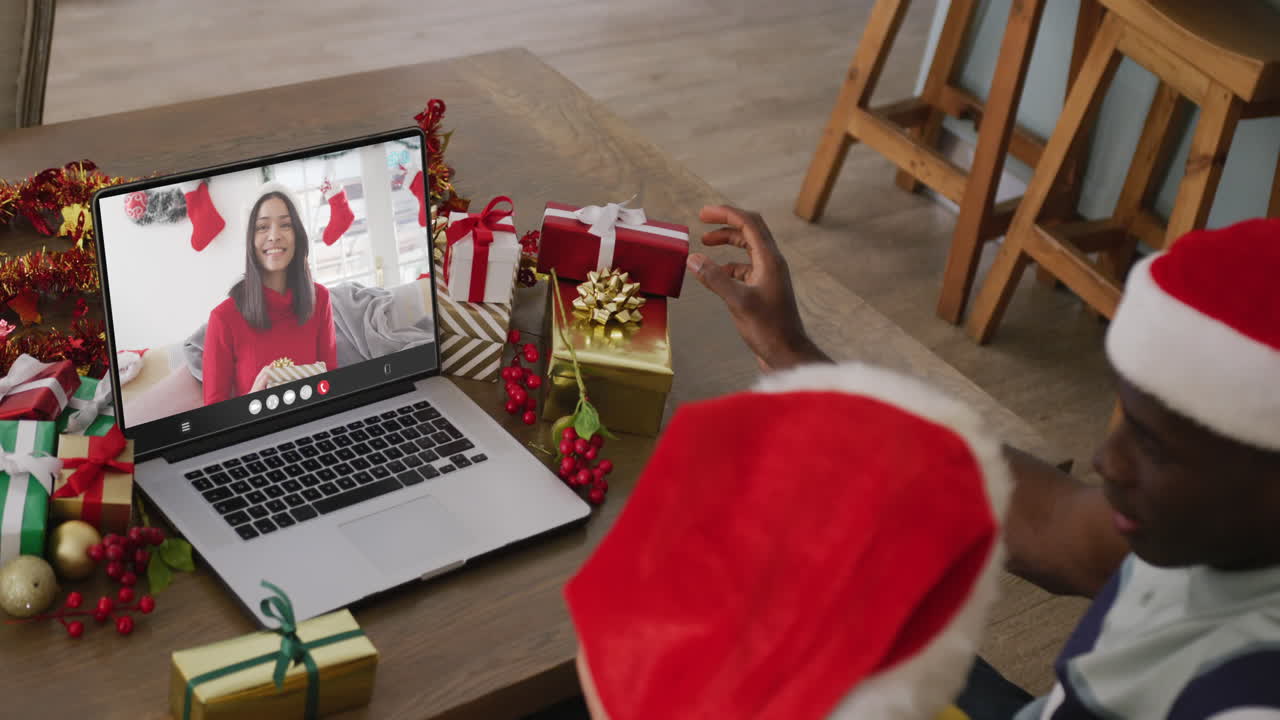pareja diversa con sombreros de santa teniendo llamada de video portátil con mujer biracial