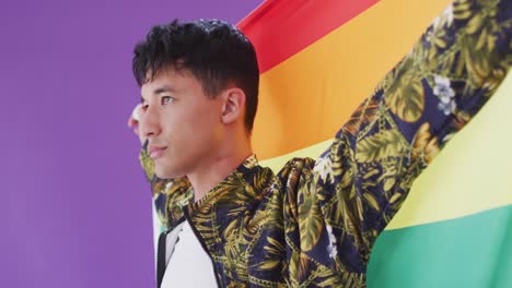 hombre biracial posando y sosteniendo la bandera lgbt con los brazos abiertos
