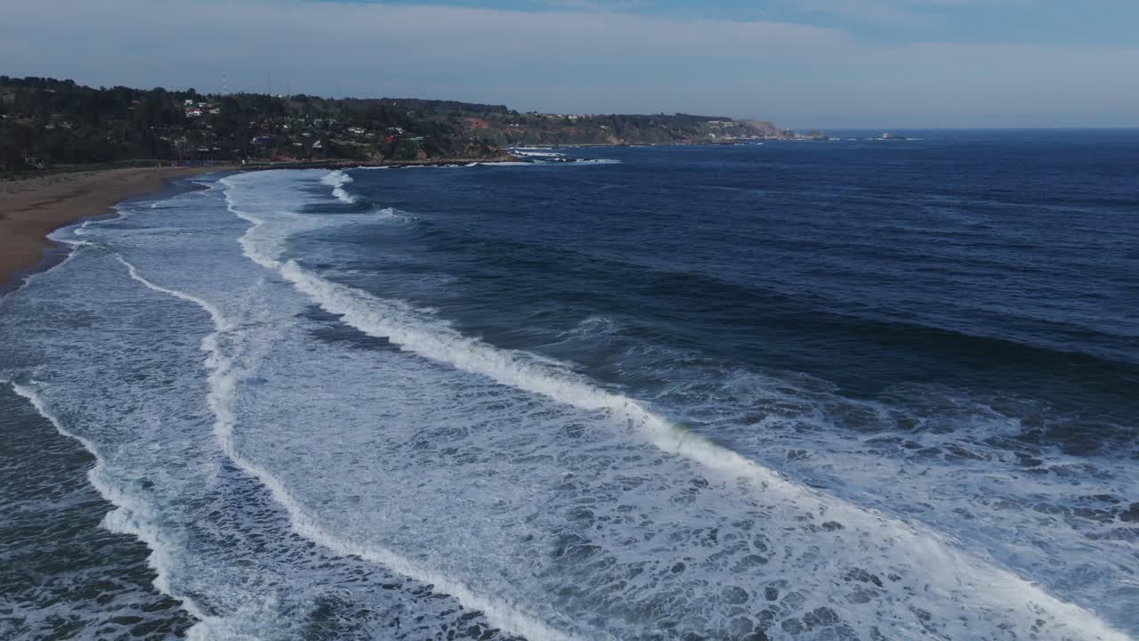 Bird's eye perspective of a solitary figure strolling along the sandy shore with waves breaking on the beach at Playa Grande, Quintay, Chile.