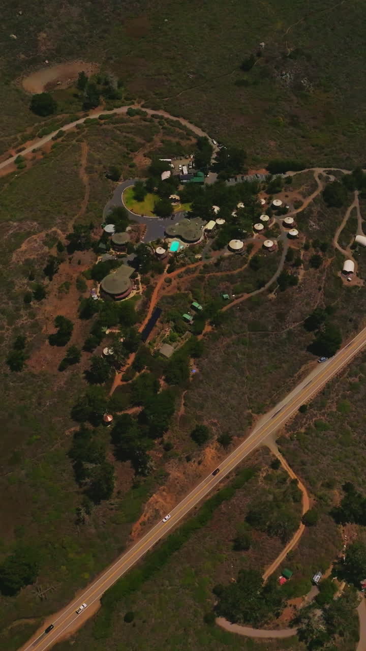 Little resort area in the mountainous territory of California coastline. Highway with cars on the edge of the rocky shore of Pacific. Top view. Vertical video