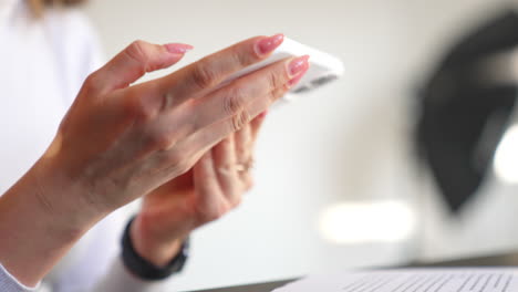 female thin hands hold white telephone. woman turns the mobile phone to take the better angle of a photo. close up.