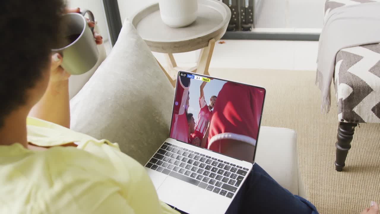 video de una persona sentada en el sofá y viendo un partido de fútbol en una computadora portátil