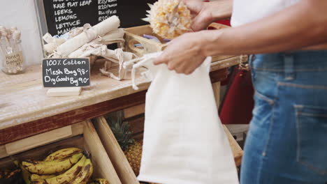 Close-Up-Of-Woman-Putting-Pineapple-Into-Reusable-Cotton-Bag-In-Plastic-Free-Grocery-Store