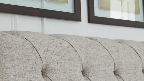 camera glides along sofa back below dark wood frames on white wall