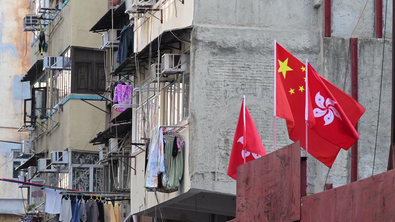 Nærbilde av Hongkongs og kinesiske flagg som vaier utenfor en gammel boligbygning i Kowloon. Illustrerer tilstedeværelsen av nasjonal identitet midt i byboernes barske hverdag.