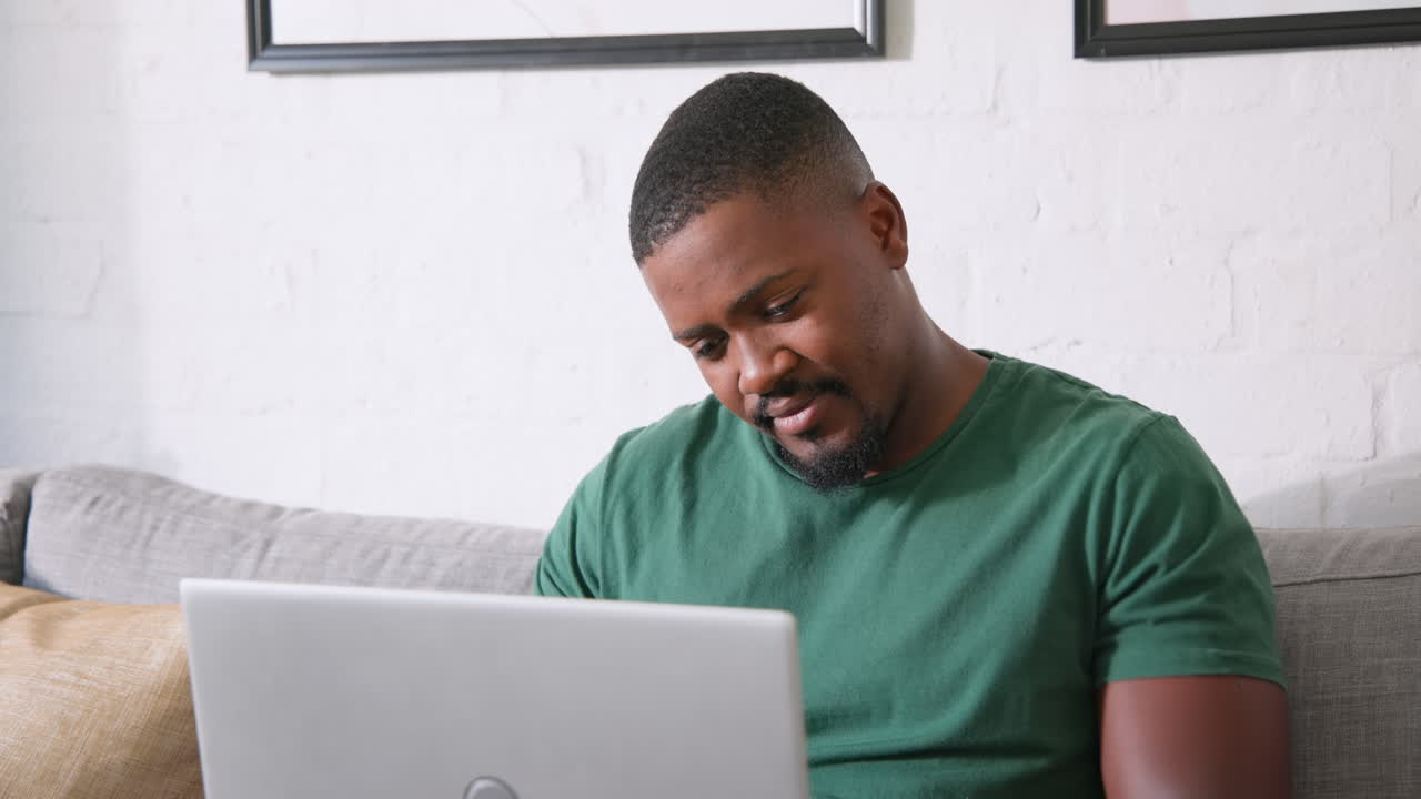 African American man using laptop at home, looking thoughtful and focused, copy space