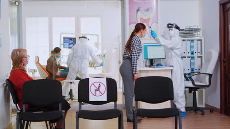 assistant with coverall measuring patient temperature