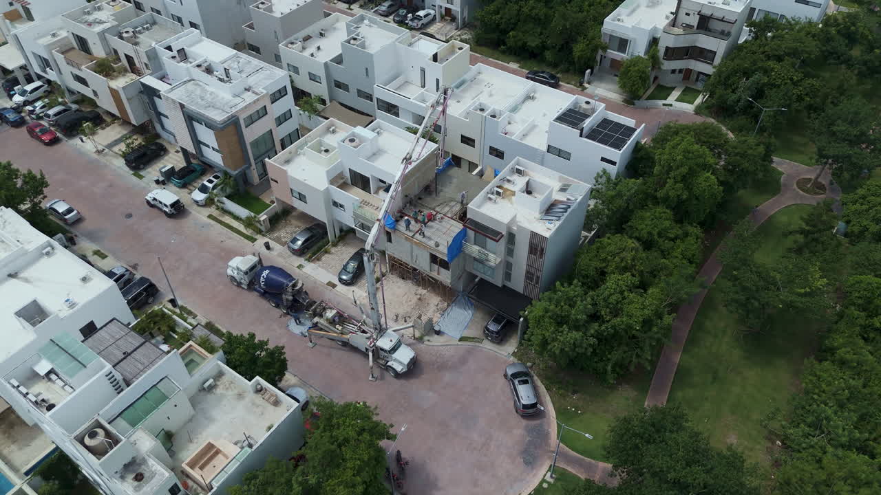 Tilt down drone shot of a concrete pump pouring cement to make the tile of a house with several workers spreading the material