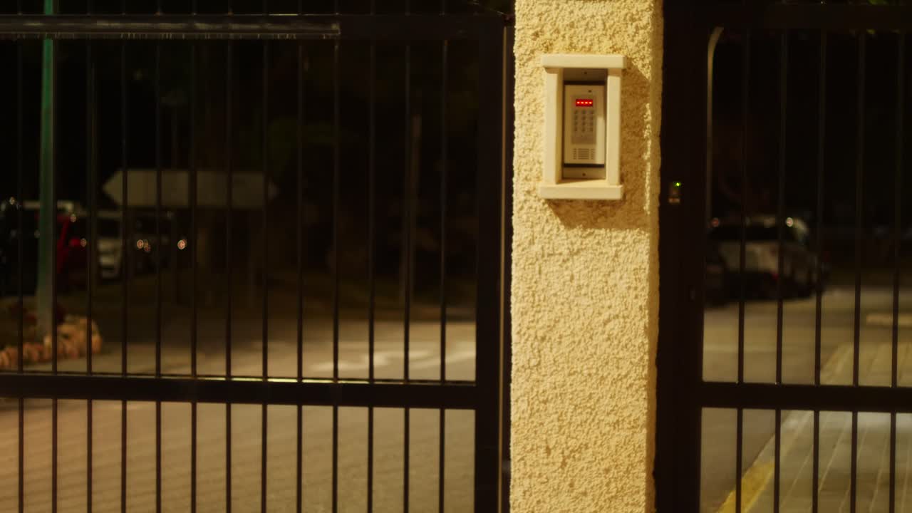 Cancello di una comunità recintata che si apre di notte all'arrivo di un'auto