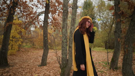 beautiful lady in the woods strolling with a yellow beret and matching muffler, adjusting her hair with her left hand while wearing sunglasses