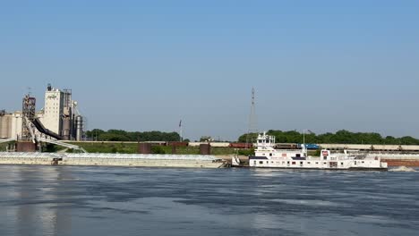 Nahaufnahme-Eines-Schleppers,-Der-Einen-Langen-Lastkahn-Auf-Einem-Glasklaren-Fluss-An-Einer-Industrieanlage-Vorbei-Schiebt