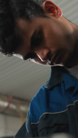 niño trabajando en una tableta en un taller industrial mientras otro hombre se centra en la tarea, el fondo presenta equipos de taller, herramientas y maquinaria