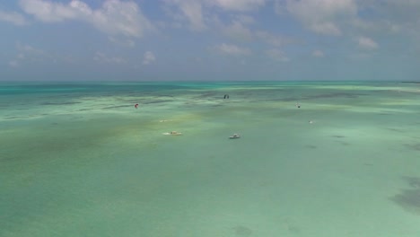 People-kitesurf-far-away-on-turquoise-sea-water-with-motorboat-stand-on-side-for-safety