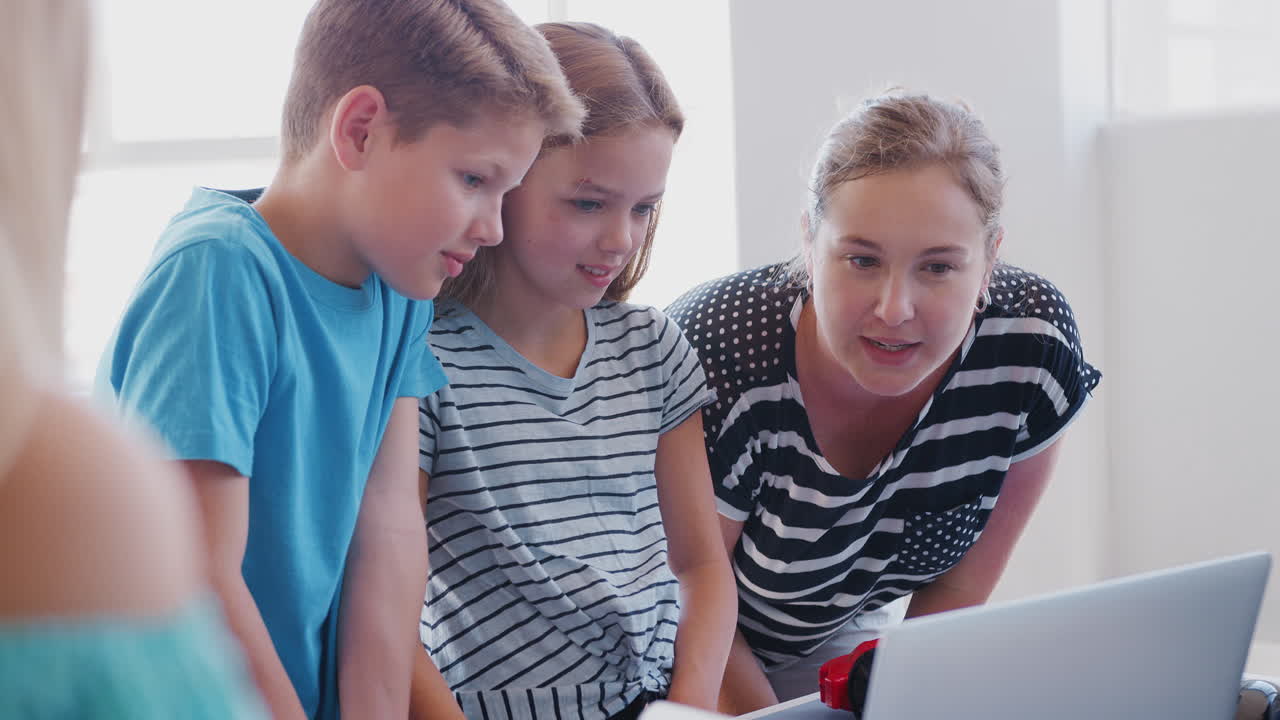 Two Students With Female Teacher In After School Computer Coding Class Learning To Program Robot Vehicle