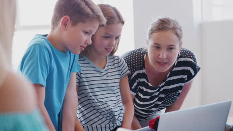 two students with female teacher in after school computer coding class learning to program robot vehicle