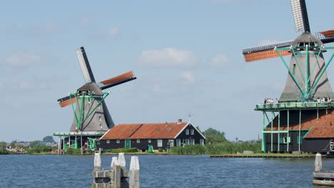 a classic dutch windmill steadily rotates beside a calm river under bright daylight, with traditional houses and blue sky in zaandam, netherlands