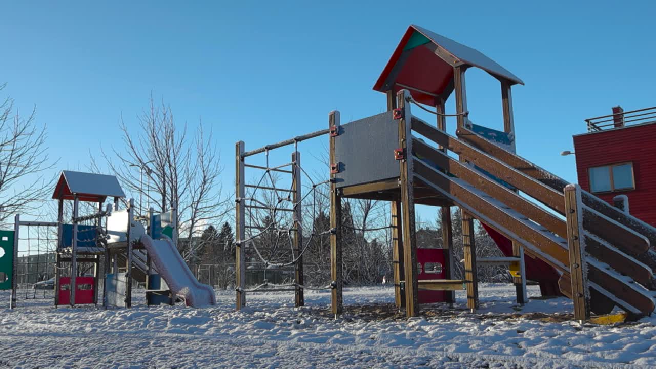 детская площадка в зимнее время солнечный день в лагри эстония с горками и аттракционами. снег покрывает землю и крыши игровой площадки, в то время как голубое небо на заднем плане.