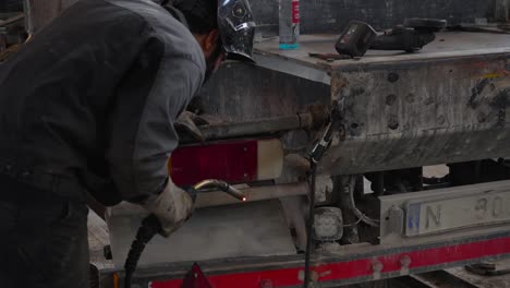 trabajador inspecciona y suelda camiones sucios en el taller