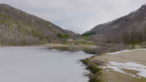 ice on frozen lake starting to melt in early spring with cabin at foothills of mountain