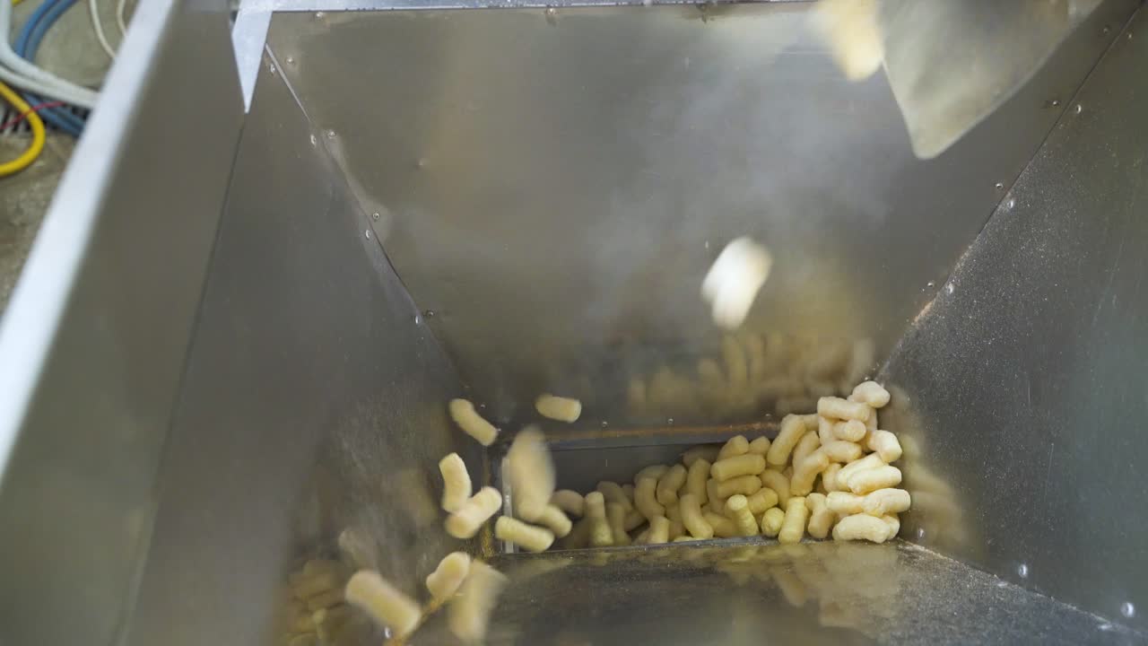 Pouring snack corn sticks into a metal container at a food factory. Automatic packaging line for products