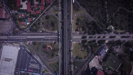 toma cenital de la intersección de la hoja de trébol al sur de la ciudad de méxico, que muestra varios autos conduciendo, un estacionamiento, canchas de fútbol en la esquina inferior derecha, árboles y algunos techos rojos