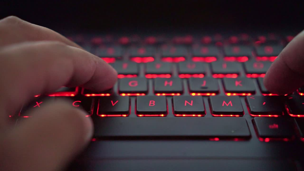 Person, der taster på et baggrundsbelyst tastatur, nærbillede, digital arbejdsplads, teknologi og online aktivitet