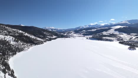 Aerial-view-of-ice-frozen-lake,-woods-and-mountain-landscape