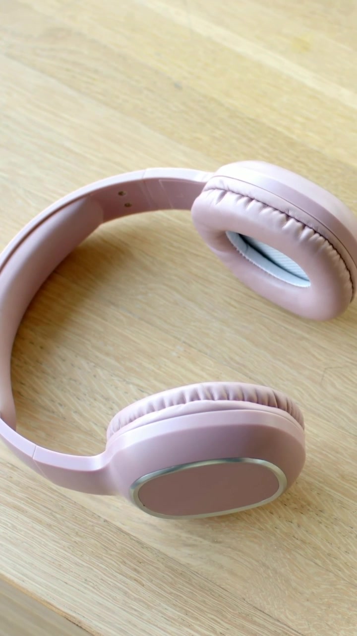 Vertikal video: Panorerende kamera avslører rosa hodetelefoner på en bordplate av tre, som viser polstrede puter.