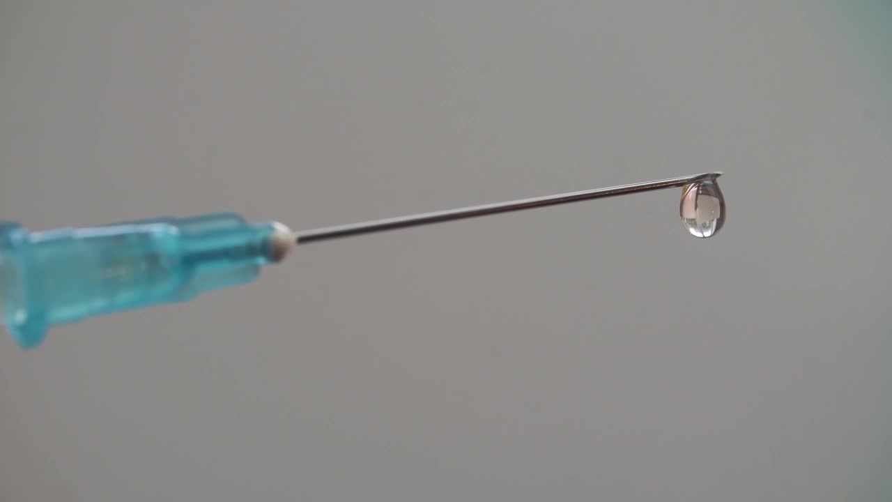 Gota de líquido transparente se formando e caindo da ponta da agulha da seringa