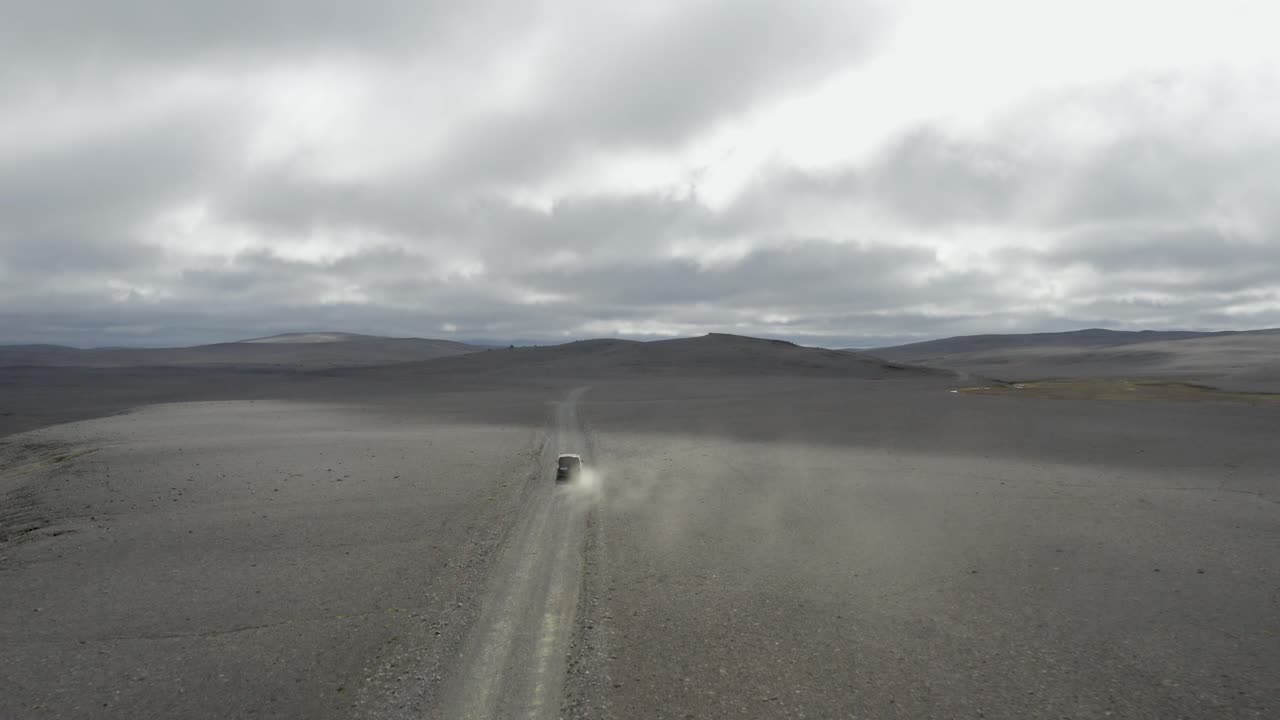 Aerial wide shot of a vast black volcanic sand desert stretching to the horizon with a vehicle and distant mountains under dramatic cloudy skies in Iceland