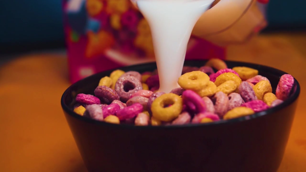 Cereali colorati in una ciotola con latte versato, al rallentatore.