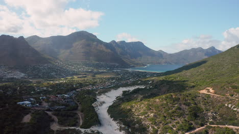 Magnífica-Vista-De-La-Playa-De-Sandy-Bay-Con-La-Ciudad-Portuaria-De-Houtbay-En-El-Fondo-En-Sudáfrica---Toma-Aérea