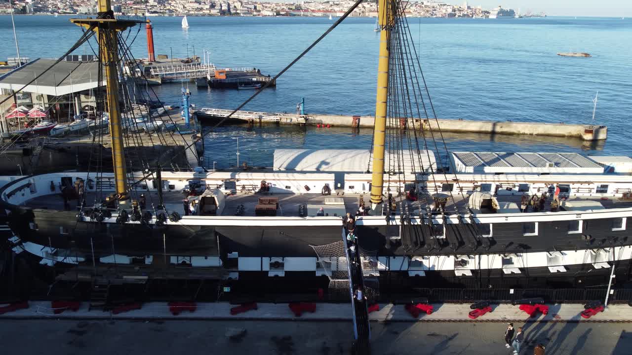 Drone shot flying sideways over an old docked Portuguese vessel.