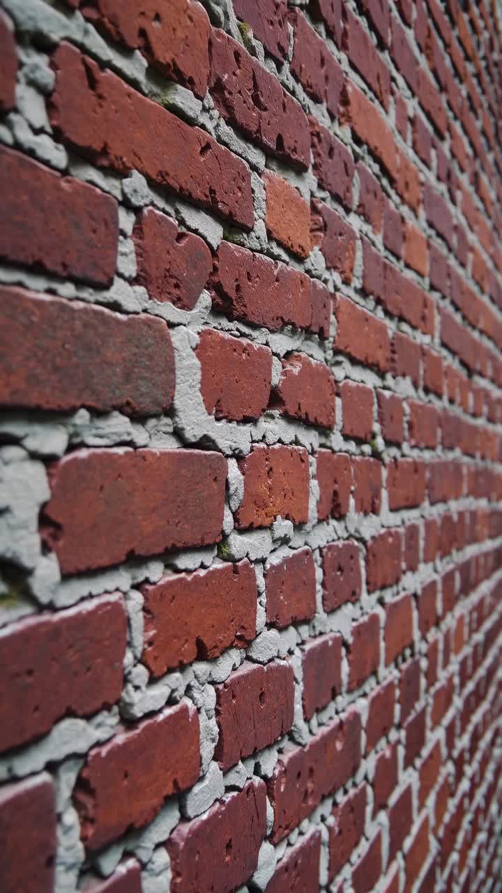 Close-up, angled view of a red brick wall with visible mortar lines, creating a textured, dynamic
