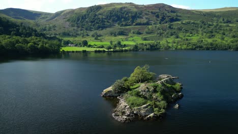 orbit of small island in dark lake with reveal of lush wooded hillsides on bright summer day