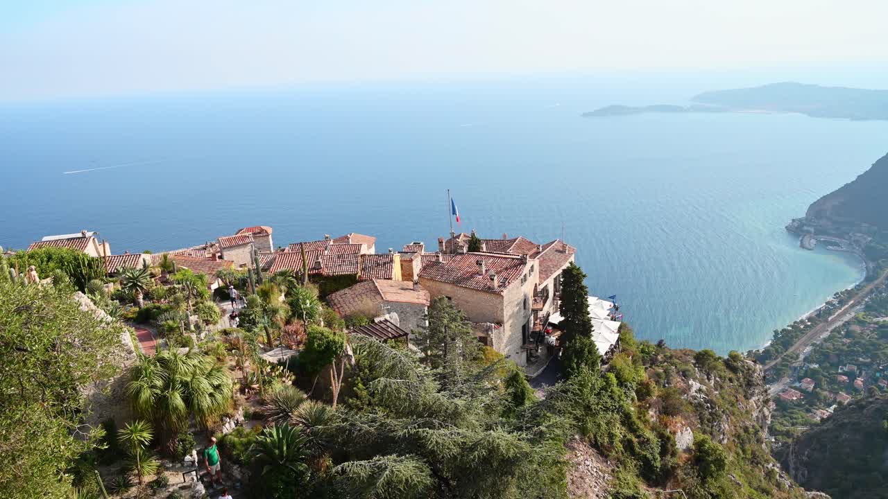 Park with tropical plants in Menton, France. People, roofs of traditional residential buildings, sea on the background