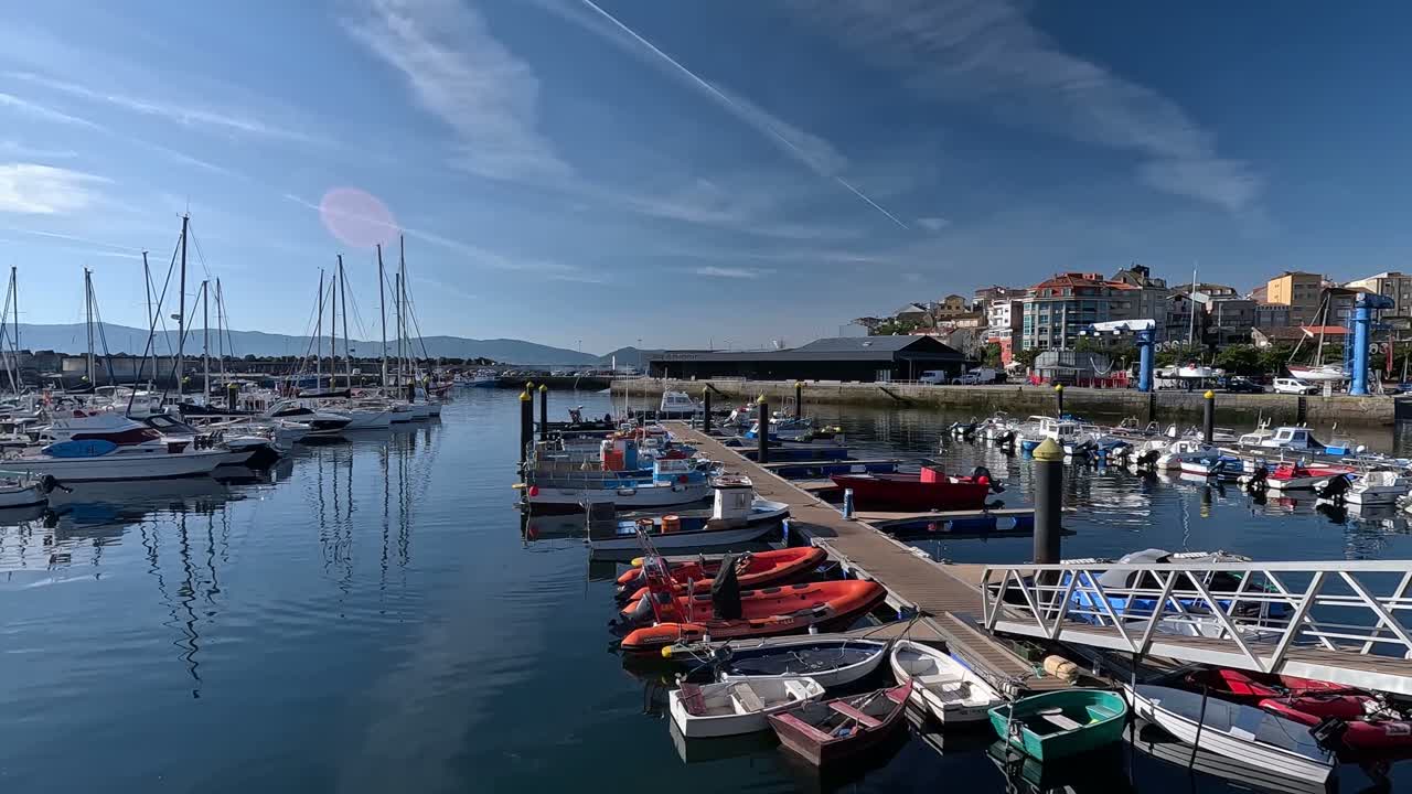 Barche da pesca ormeggiate di fronte a yacht turistici nel porto calmo poco dopo l'alba in una giornata estiva con sole splendente, ripresa descrittiva con movimento verso sinistra.