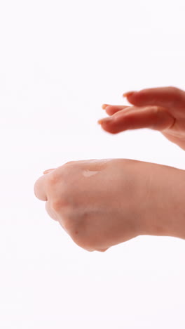 vista aérea de las manos aplicando una gota de líquido a la parte posterior de una mano contra un fondo blanco