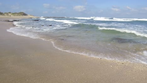 waves break on the beach as a couple walk by in the distance