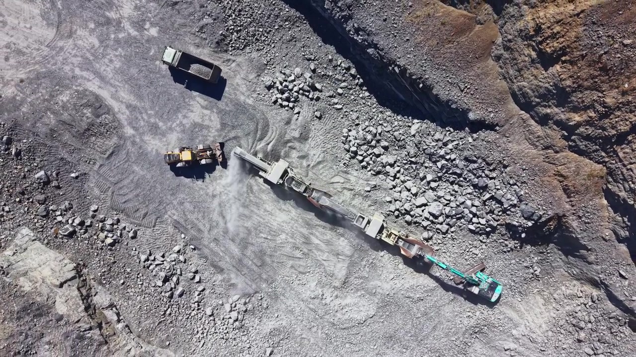 Granite quarry work takes place with heavy machinery and trucks moving materials in a busy extraction site