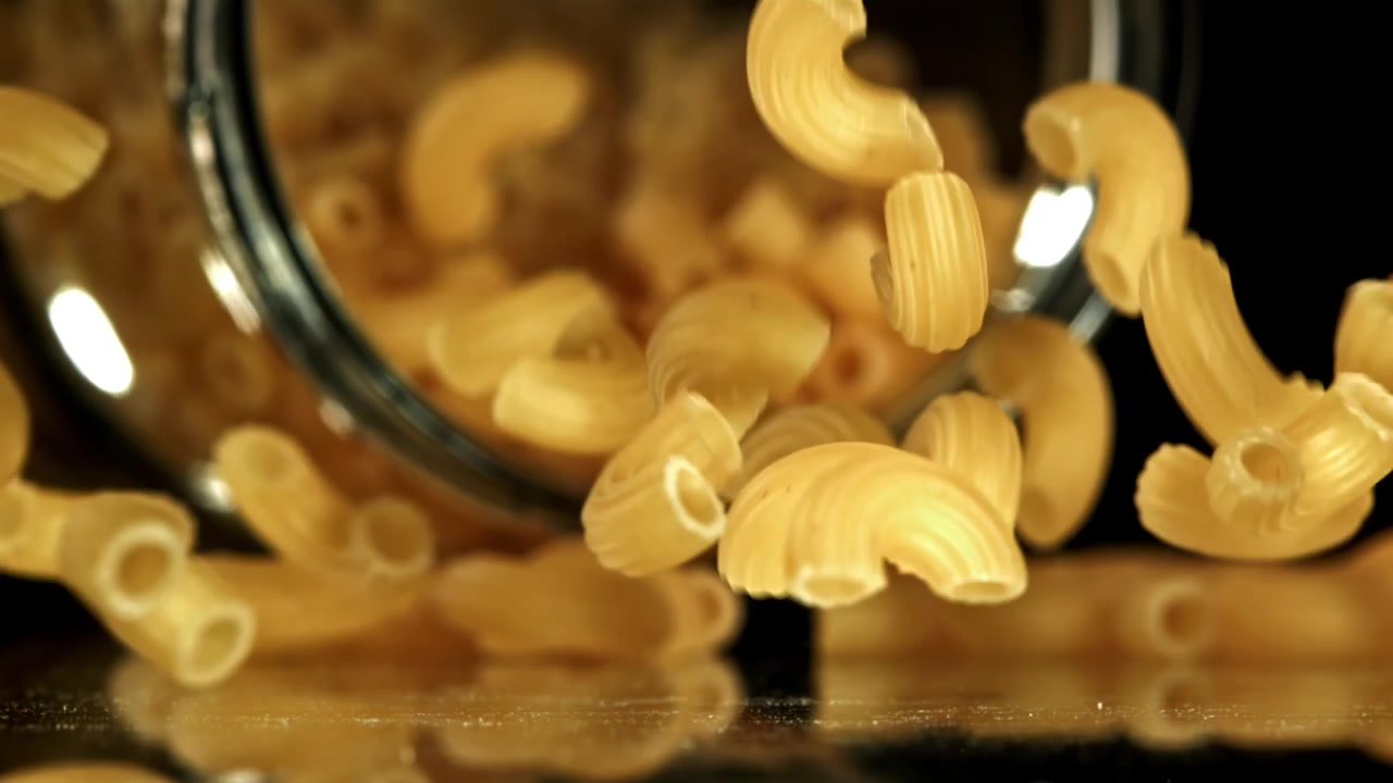 Pasta maccheroni secca che cade da un barattolo di vetro al rallentatore