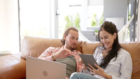 una pareja diversa está usando una tableta en un sofá en casa