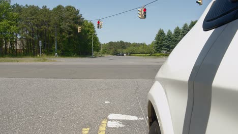 white car pulls up to traffic light and stops, during the day, with driver's side of car and wheel in the shot