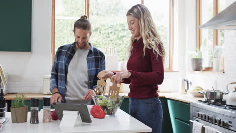 Feliz-Pareja-Diversa-Preparando-La-Cena-En-La-Cocina-Usando-Una-Tableta-En-Casa,-En-Cámara-Lenta