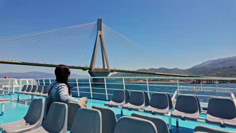 Woman-on-a-ferry-admiring-the-Rio-Andirrio-Bridge-in-Greece-on-a-clear,-sunny-day