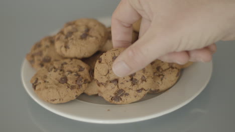 mano colocando galletas con trocitos de chocolate en un plato blanco - ángulo alto