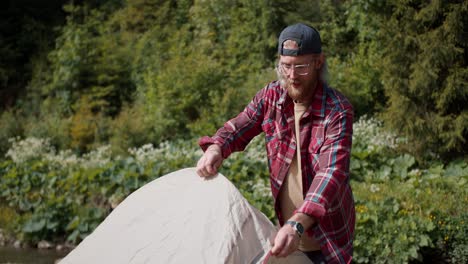 Shooting-near-a-blond-man-with-a-beard-in-glasses-in-a-red-plaid-shirt-lays-out-and-sets-up-a-tent-against-the-backdrop-of-the-forest