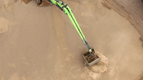 aerial view of a green arm moving sand, creating a cloud of dust in a sandy excavation site