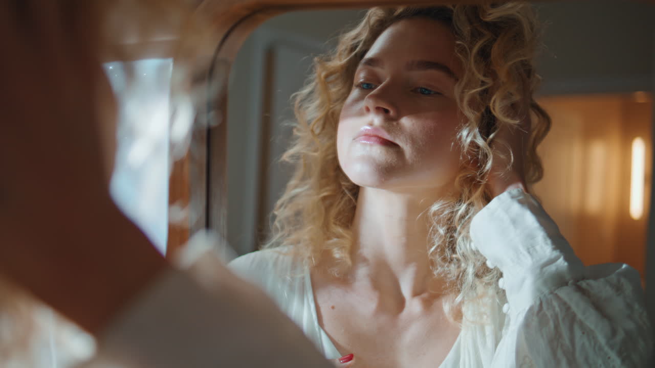 Closeup woman examining face in reflection. Smiling curly girl admiring beauty
