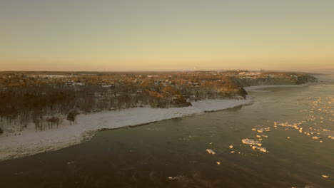 Vista-De-Drones-Yendo-Hacia-La-Costa-De-La-Ciudad-Canadiense-De-Beaumont,-Quebec,-Desde-La-Vía-Marítima-Del-Río-San-Lorenzo,-En-Una-Mañana-De-Invierno-Muy-Fría